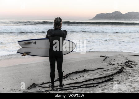 Un surfeur de St James sur Danger Beach envisage de retourner dans la mer tout en regardant une autre série de vagues sur la péninsule du Cap, Afrique du Sud Banque D'Images