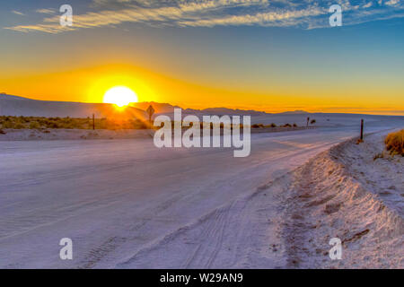 Excursion Sur La Route Du Désert. Magnifique coucher de soleil dans le désert avec route rurale reculant à travers les dunes de sable du monument national de White Sands au Nouveau-Mexique. Banque D'Images