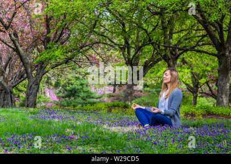 Jeune femme assise dans un parc méditant dans une pose de yoga. Banque D'Images