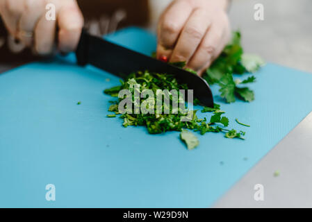 La jeune fille coupe verts, oignons, persil et divers assaisonnements avec un couteau sur une planche à découper. Femme cuire salade pour la cuisson. Banque D'Images