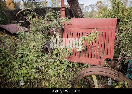 Anciens abandonnés le tracteur dans le champ. Terrain agricole avec rouillé vintage tracteur dans un champ couvert de végétation. Banque D'Images