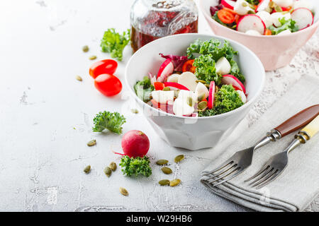 Salade de laitue Iceberg, Kale et Radiccio, tomates cerises, radis, mini-mozzarella et les graines de citrouille dans des bols sur un fond clair Banque D'Images