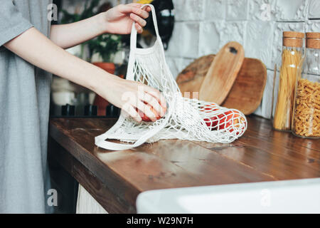 Jeune femme tire les pommes de chiffon tricot chaîne sac shopper Sac dans la cuisine, zéro déchet, slow life Banque D'Images