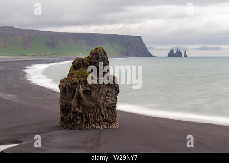 Sur la plage de Reynisfjara qui jouit de Lone Rock (vue de l'Kirkjufjara , le sud de l'Islande) la péninsule de Reynisdrangar avec au loin. Banque D'Images