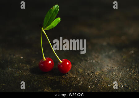 Paire de cerises avec des feuilles vertes sur l'ancien, de la pierre, marbre rustique. Banque D'Images
