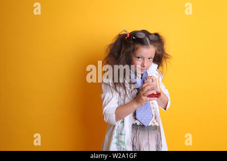 MR - Science Geek Jeune fille / Femme Age 7 looking at camera holding bécher en verre borosilicaté, produits chimiques sciences rouge sur fond jaune avec copyspace Banque D'Images