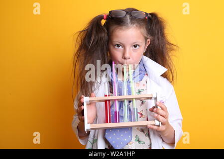 MR - Science Geek Jeune fille / femme - 7 ans - enfant buvant dans des tubes à essai avec de la paille à l'appareil photo sur fond jaune Banque D'Images