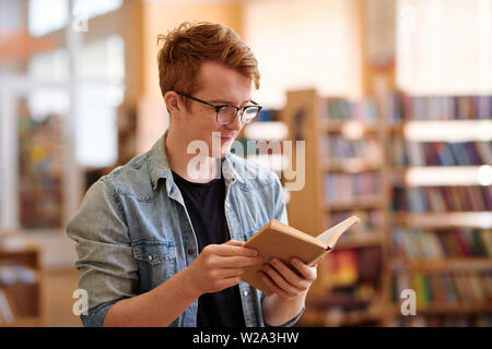Jeune étudiant en chemise en jean noir et tee reading book Banque D'Images