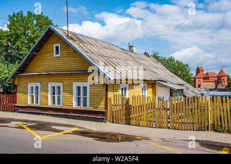 Vilnius / Trakai, Lituanie - le 7 juillet 2019 : Ancienne maison jaune en bois traditionnel lituanien avec trois fenêtres et château médiéval et le lac sur le backg Banque D'Images