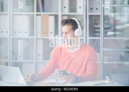Casual young businessman dans l'aide d'écouteurs gadgets modernes Banque D'Images