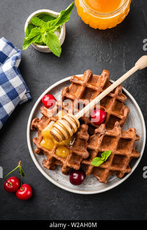 Gaufres Belges sain de blé entier avec du miel et cerises sur fond noir, la plaque de table en béton, sur un aliment sucré ou dessert Banque D'Images