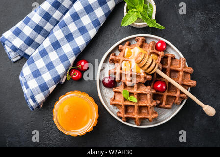 De délicieuses gaufres belges avec le miel, les cerises sur une plaque béton noir, arrière-plan. Dessert sucré ou petit-déjeuner. Vue d'en haut Banque D'Images