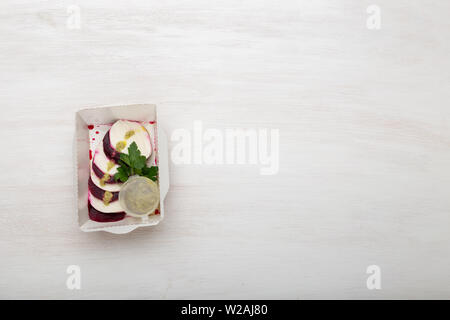 Vue de dessus de betteraves bouilli avec des tranches de fromage blanc se trouvent dans une boîte à lunch blanc avec sauce à la crème aigre et le persil sur un tableau blanc à côté de fromage de chèvre Banque D'Images