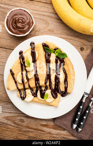 Crêpes à la banane et sauce au chocolat sur plaque blanche en bois rustique, arrière-plan. Vue de dessus de table Banque D'Images