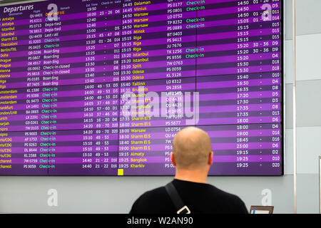 Un homme est debout devant le conseil d'information pour les arrivées et départs. Le stand d'information à l'aéroport, gare, station de bus, voyage Banque D'Images