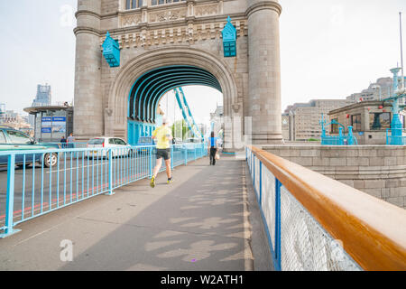 Londres, ANGLETERRE - 16 juillet 2013 ; l'architecture historique de Tower Bridge avec femme marche en avant de l'homme dans l'ensemble jogging brouillée. Banque D'Images