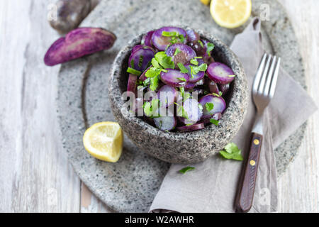 Chilotan cuisine chilienne de l'île. Salade de pommes de terre pourpre violet avec du citron, l'oignon de printemps et la coriandre dans un bol en pierre. Fond gris. Banque D'Images
