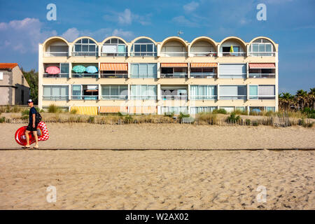 Seul homme à marcher le long de la promenade de la plage en face de certaines années 1980 Holiday Apartments Banque D'Images