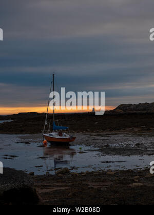 Conseil informatique, Pays de Galles, Royaume-Uni - un bateau est mise à la terre une marée basse sur les rochers alors que le soleil se couche sur la mer. Banque D'Images