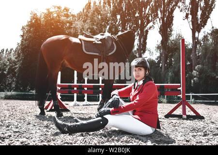 Jeune fille jockey et son cheval posant après la formation. Elle aime les animaux et joyeusement passe son temps dans leur environnement. Banque D'Images