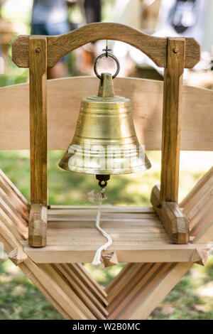 Métalliques en laiton médiévale Bell et la construction en bois pour utilisation à la main et en sonnerie sur une chaise en bois et arrière-plan flou. Cité médiévale et historique Banque D'Images