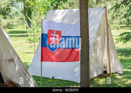 Drapeau de la Slovaquie et camp tente dans une forêt dans la nature sur une journée ensoleillée. Camping et rétro tente sous ombre d'une forêt de pins en Europe Banque D'Images