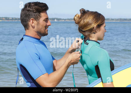 Guy aidant une jeune fille s'habillant avec wetsuit Banque D'Images