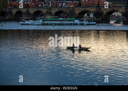 Les pêcheurs de petits bateaux de pêche près du pont Charles à Prague sur fond d'une embarcation de plaisance au coucher du soleil. Prague. République tchèque Banque D'Images