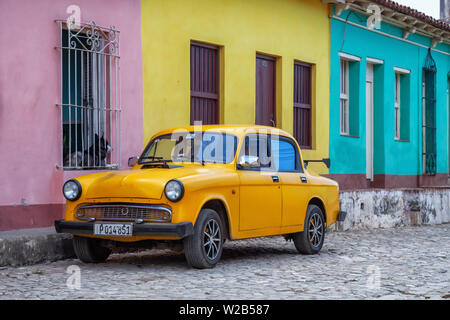 Trinidad, Cuba - 6 juin 2019 : Vieille voiture jaune avec des bâtiments colorés en arrière-plan dans une petite ville de Cuba pendant une journée ensoleillée. Banque D'Images