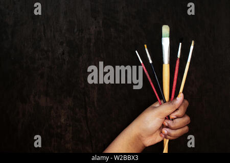 Brown Skin Girl Holding Pinceaux Peinture sur bois noir fond Conseil Banque D'Images