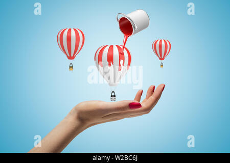 Trois petits ballons à air chaud au-dessus de la main de femme sur fond bleu clair et la peinture peut couler dans l'air de la peinture rouge sur ballon central. Banque D'Images