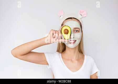 Portrait of a young woman applying avocat naturel masque sur son visage sur fond blanc. Soins de la peau et des soins spa à domicile ou salon de beauté Banque D'Images