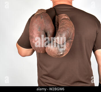 Athlète masculin détient une paire de gants de boxe vintage très ancien sur son dos, fond gris Banque D'Images
