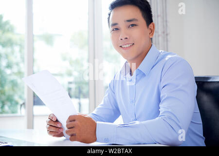 Portrait of handsome Young Asian Woman avec le document en main assis à table office Banque D'Images