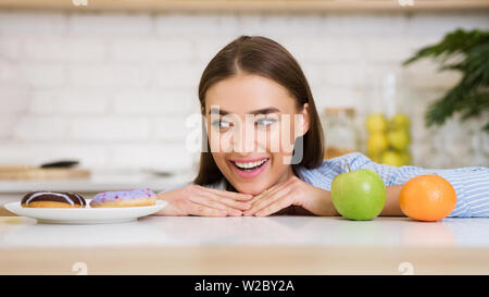 Femme de choisir entre les fruits et les sucreries, regardant donut Banque D'Images