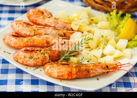 Grandes crevettes grillées avec des pommes de terre sur la plaque blanche dans un restaurant sur la table. Banque D'Images