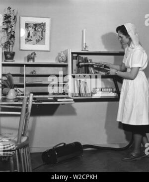 L'aspirateur dans les années 1950. Le jeune étudiant Gertrud Larsson est d'avoir une journée de nettoyage dans son appartement d'étudiants. Elle est minutieuse et même les livres de l'étagère obtient une bonne aspiration. Suède 1954 Banque D'Images