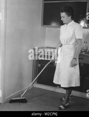Journée de nettoyage dans les années 1950. Une jeune femme habillée d'une tenue de nettoyage pratique, est le nettoyage de la cuisine et est à l'aide d'un pinceau avec une poignée télescopique. Une nouvelle invention pour se tenir bien droit lorsque la poussière et éviter les douleurs au dos. Suède 1950 Banque D'Images