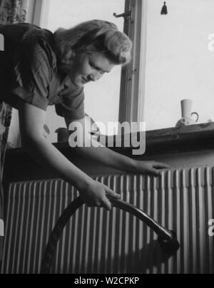 Journée de nettoyage dans les années 40. Une jeune femme est le nettoyage de son appartement et est l'aspirateur le radiateur sous la fenêtre. Suède 1948 Banque D'Images