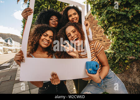 Heureux amis féminins posant avec cadre photo vide. Smiling girls avec cadre photo vide à l'extérieur de la ville. Banque D'Images