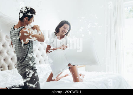 Young couple having a pillow fight dans leur chambre à coucher. L'homme et la femme se battre avec des oreillers au lit. Banque D'Images
