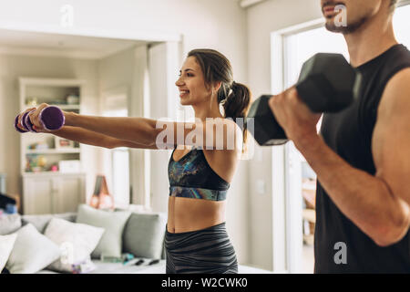 Jeune couple en bonne santé faisant des exercices avec haltères à la maison. Fit young woman with man doing entraînement poids à l'intérieur dans la salle de séjour. Banque D'Images