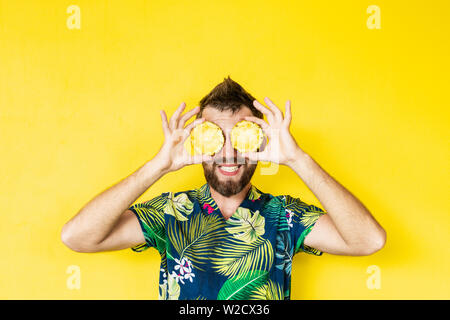 Young Caucasian man holding barbu ananas tranches de devant ses yeux, rire Banque D'Images