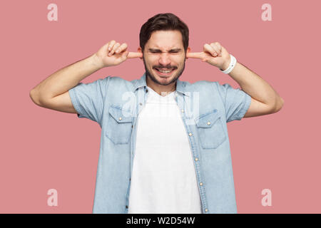 Je ne veux pas vous entendre. Portrait de confondre beau jeune homme barbu en bleu style casual shirt debout et mettre les doigts sur les oreilles et ne location Banque D'Images