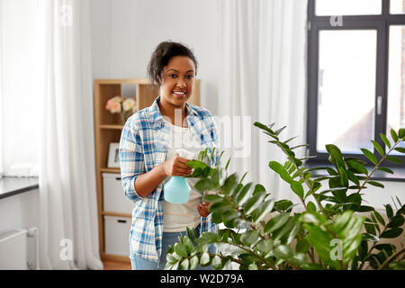 Happy woman spraying plante avec de l'eau à la maison Banque D'Images