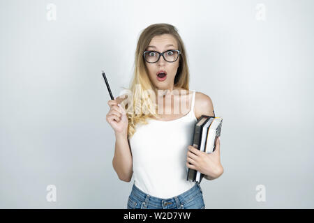 Jeune femme surprise dans les verres enclos dans une main et livres dans son autre main isolé sur fond blanc Banque D'Images