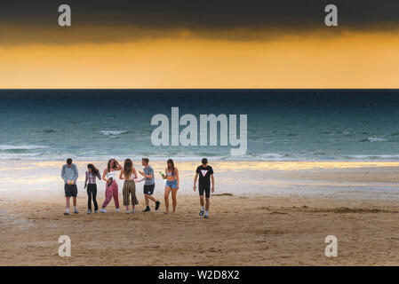 Un groupe d'adolescents traînant sur la plage de Fistral pendant un coucher de soleil spectaculaire à Newquay en Cornouailles. Banque D'Images