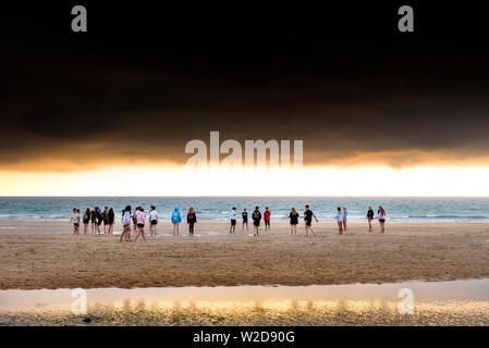 Un groupe d'adolescents flâner sur la magnifique plage de Fistral au coucher du soleil d'or à Newquay en Cornouailles. Banque D'Images