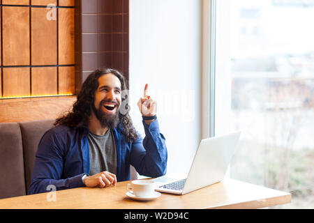 J'ai idée ! Portrait of happy confiant beau jeune homme adulte freelancer dans style casual assis dans un café avec un ordinateur portable, montrant doigt vers le haut avec la dent Banque D'Images