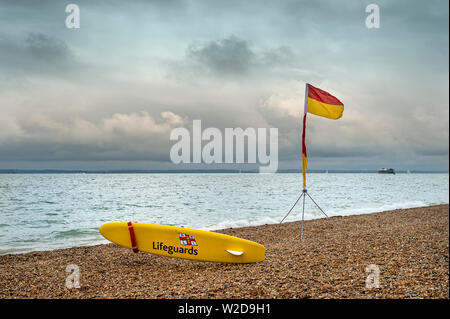 Sauveteur RNLI conseil jaune et rouge et jaune sont sûrs d'un drapeau sur une plage de galets. Banque D'Images